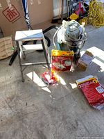Shop Vac with electrical cord and hose, disposable filter bags, boxed part, and aluminum 2-step ladder in garage setting