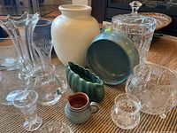 Photo showing overall lot: green Lucia Ware ceramic flower bowl, various crystal and glass vases, crystal covered jar, ceramic cup, arranged on woven mat