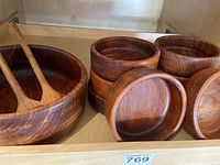 Photo showing the large teak salad bowl with wooden salad utensils inside and a stack of eight teak side bowls beside it, illustrating bowl shapes and wood grain detail.
