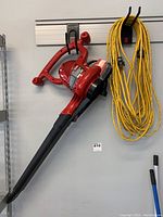 Red Toro electric leaf blower hanging on wall with attached cord, alongside a coiled yellow extension cord.