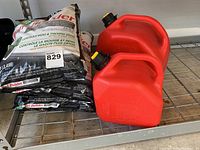 Three bags of Scotts Turf Builder placed side by side on a metal shelf, next to two red jerry cans.