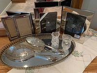 Photo showing the complete collection of silver ornate tray, hairbrush, mirror, two small crystal vessels, silver picture frames, and embroidered tablecloth.