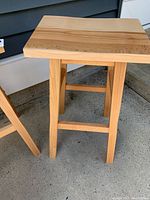 Light colored wooden stool showing rectangular wooden seat and legs