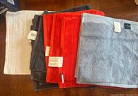 Stack of washcloths showing multiple colors including white, grey, orange, and blue, folded square and stacked horizontally.