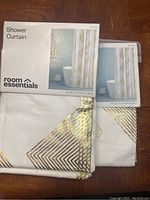Photo of two packaged Room Essentials shower curtains with white cotton material and gold foil geometric designs, showing brand and packaging.