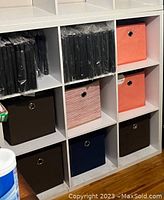 Shelving unit displaying 11 fabric foldable storage cubes in various colors including brown, navy blue, coral and pink striped.