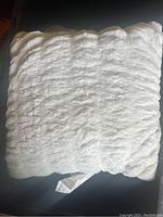 Top view of a single off-white furry square throw pillow, showing texture and size.