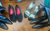 Four pairs of women's shoes arranged on wooden floor: two pairs of mid-calf black boots, one pair of black heels with ankle strap, and one pair of black Skechers slip-ons.