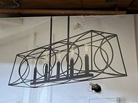 Photo of chandelier with rectangular geometric metal frame and five candle-style lights on a linear bar, matte black finish.