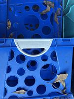 Close-up image showing blue plastic milk crate with circular holes and built-in handle.