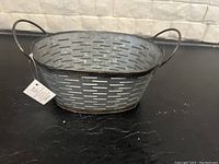 Gray metal oval tray with side handles and perforated design on black surface