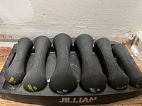 Six Jillian Michaels dumbbells arranged on branded stand, weights range 3-8 lbs