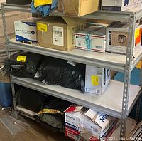 Photo showing assembled garage storage shelf with various boxes and bags placed on shelves. Shelves are white, frame is grey metal.