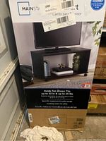 Photo showing the Mainstays TV stand in packaging featuring a TV on top and description of features.