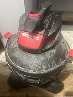 Front angled view of Shop Vac wet/dry vacuum cleaner showing the red and black top with handle on a dusty surface.
