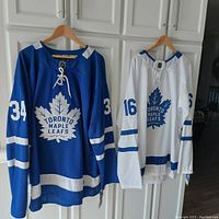 Front view of blue Auston Matthews and white Mitchell Marner jerseys hanging on hooks