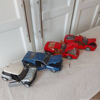 Four Maisto 1:24 scale model cars lined up on a white surface, showing their open hoods and doors