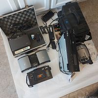 Overview photo of all items showing video camera, batteries, charger, tapes, radios, DVD player, and cases.