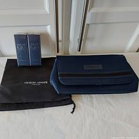 Photo of the navy blue Giorgio Armani travel pouch next to the black dust cover bag and two boxed Acqua di Gio Profondo sprays.