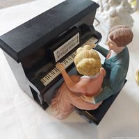 Front angle view of a music box featuring a man and woman seated at a black piano keyboard.