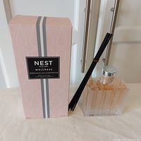 Photo of the boxed diffuser set next to the glass diffuser bottle with inserted black reed sticks showing the contents and packaging.