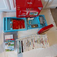 Overall lot arranged on table: red console, original box, accessories, manuals and game cases laid out