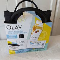 Front angled photo of sealed Olay Hello Hydration gift set showing box with visible text and partial view of included tote bag handle.