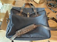 Exterior view showing navy canvas material, brown leather handles, flap cover, and front pocket.