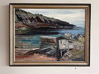Framed acrylic painting showing a coastal rocky shoreline with dock and wooden buildings, signed by artist Kelsey Raymond.