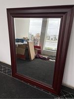 Full view of large rectangular mirror with dark wood frame leaning against a wall.