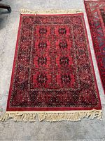 Full view of red Persian style viscose area rug with intricate black and cream patterns and fringed edges.