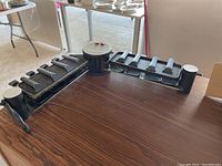 Eight-person swivel raclette cooking set, viewed from above showing black arms with eight small pans and central circular heating element with power indicator lights.
