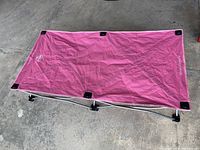Toddler nap cot with pink fabric cover laid flat on the ground, showing frame and fabric surface.