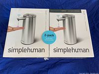 Front of two Simplehuman touch-free sensor soap dispenser boxes, each showing dispenser dispensing soap onto a hand, labeling indicating 2-pack and brand name simplehuman