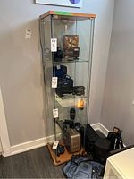 Front and slightly angled view of clear glass display cabinet with wooden top and bottom. Shows internal shelves and empty interior.
