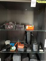 Overview of lot on two glass shelves showing Konica SLR, video camera, Nikon Coolpix, and accessories below