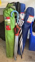 Photo showing two green Ventura boarding style camping chairs in carry bags, and three golf size umbrellas in different covers.