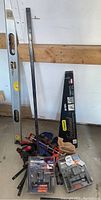 Full view of lot showing the hand saw, level, various bar clamps and pipe clamp, packaged hardware, and caulking pump arranged against a wall.