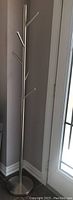 Full view of the tall polished metal coat rack standing next to a wall and a door.
