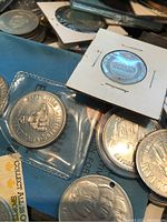 Close-up showing detailed 1988 Calgary Olympic commemorative coin and other large silver-toned coins in sleeves and holders