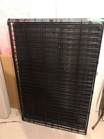 Folded black coated metal wire dog crate showing folded condition and plastic tray inside