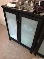 Front view of dark laminate cabinet with two vertically ribbed frosted glass inset doors and silver handles showing clothes hampers inside.
