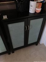 Front view of dark laminate cabinet with two ribbed glass inset doors and curved metal handles, closed.