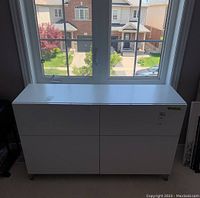 Front view of white IKEA four drawer dresser seen under a window.
