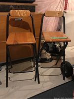 Photo showing two IKEA Dennis model folding bar stools with solid wood seats and backs and black metal frames in basement.