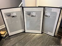 Three black IKEA Ribba frames standing on floor with original labels on the glass showing 61x91 cm (24x36 inches) dimensions.