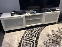Front view of white IKEA media unit with TV and various items on top, showing overall design and size.