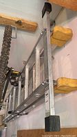 Twelve-rung aluminum articulated ladder hung horizontally on wall with visible black plastic end caps and stabilizing feet.