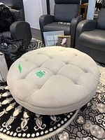 Top view of the round tufted ottoman with beige fabric upholstery and visible tufting buttons, placed on a patterned rug.