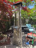 Front view of large metal outdoor patio heater standing on patio, showing full height and surroundings.